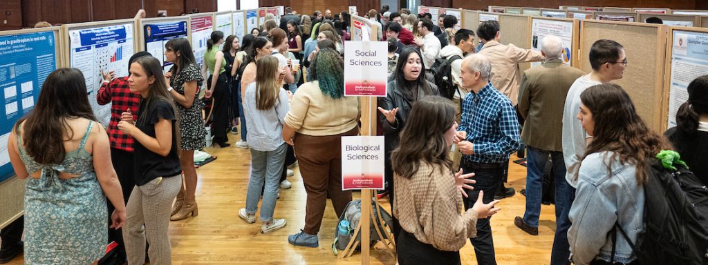 Students presenting their research at a poster session in a crowded hall
